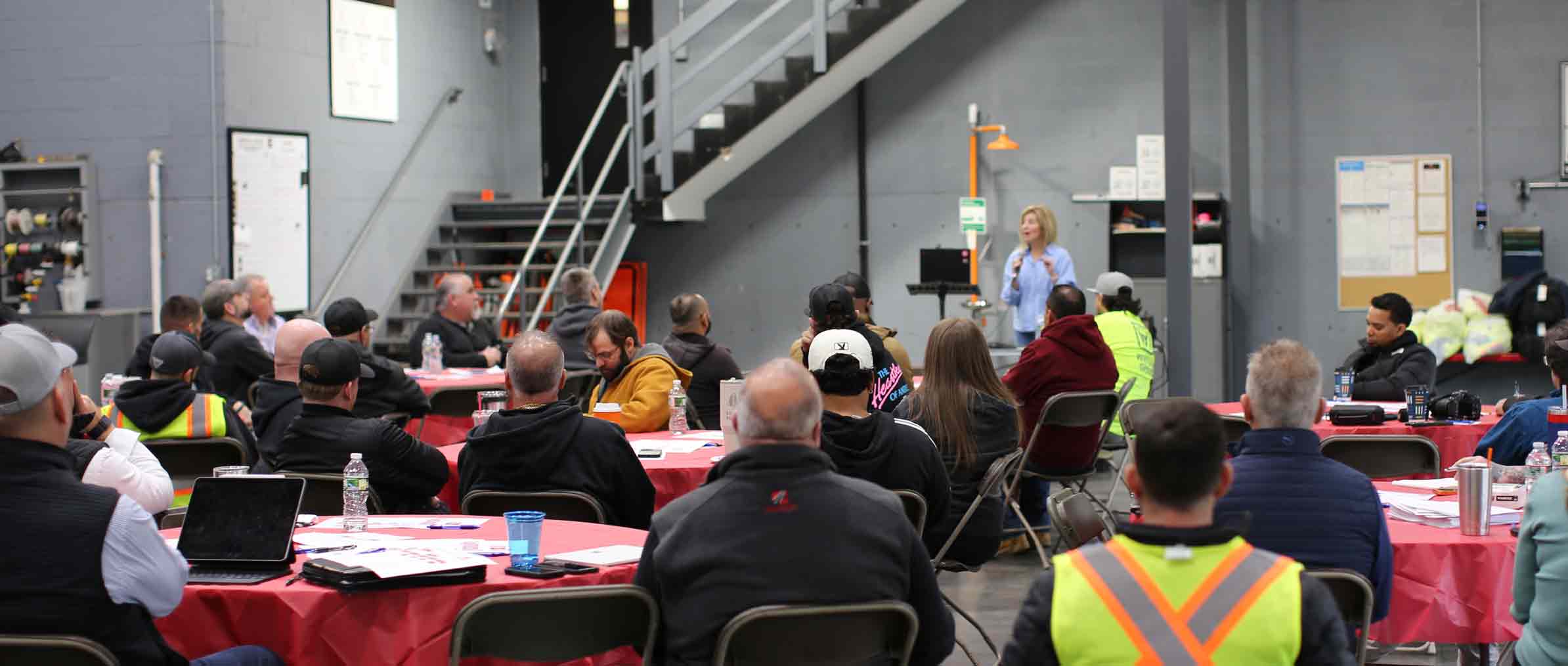 Julie Gowthorpe speaking to a group of workers seated at round tables during a workplace training session at Cassidy Paving in Boston.